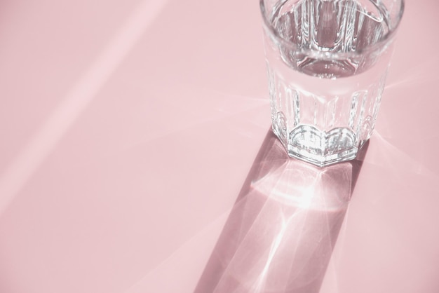 Glass of water on pink sunlight and shadow copy space