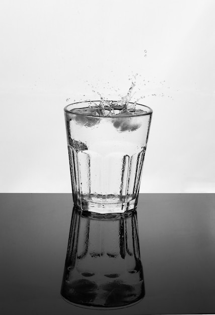 Стакан воды на отражающей поверхности, брызги капель на белом фоне, напитки и концепция гидратации