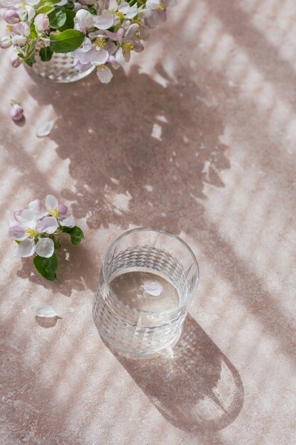 Glass of water on the table with blossoming apple tree branch in a glass