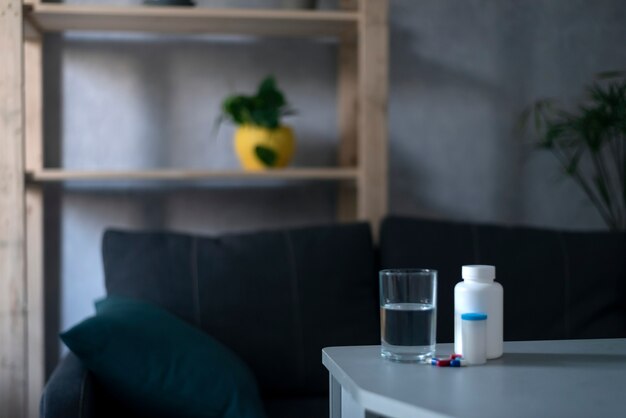 Glass of water and two bottle of pills on table in empty living room. Health concept, treatment.