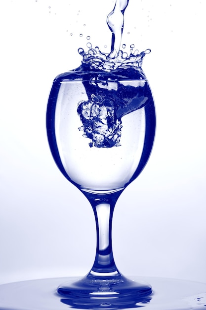 Glass of water. Water Splash in wine glass on blue background