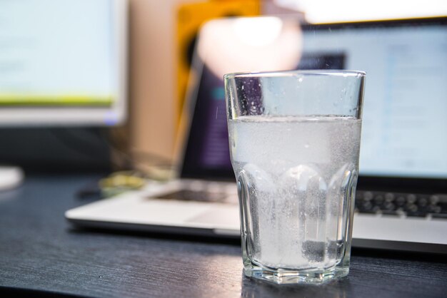 Glass of water with aspirin. laptop on background. overloaded with office work