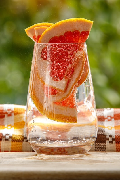 A glass of water with grapefruit in the garden background.