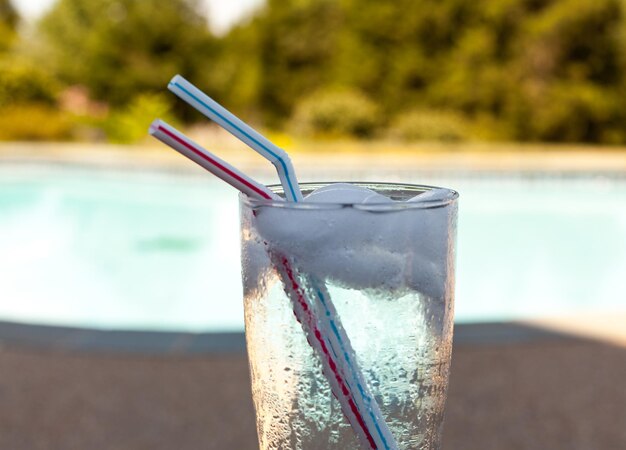 Glass of water with ice cubes on side of pool