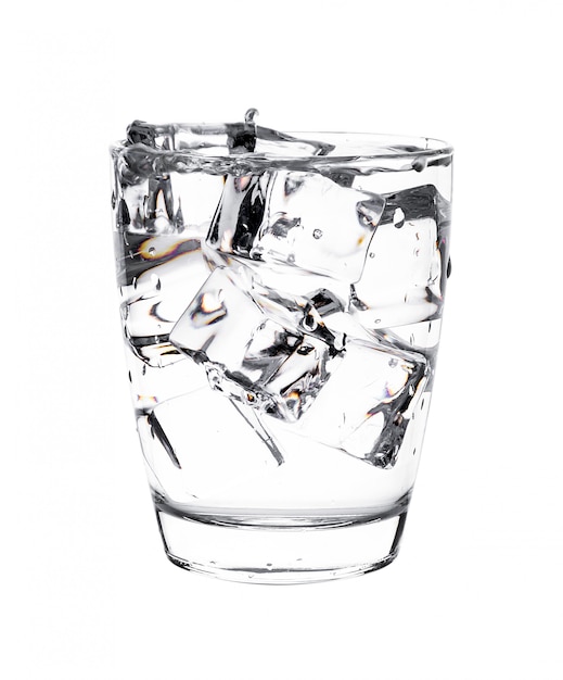 Glass of water with ice cubes on white wall