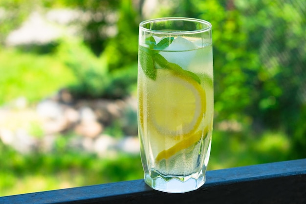 A glass of water with lemon and mint on the background of fresh summer green grass