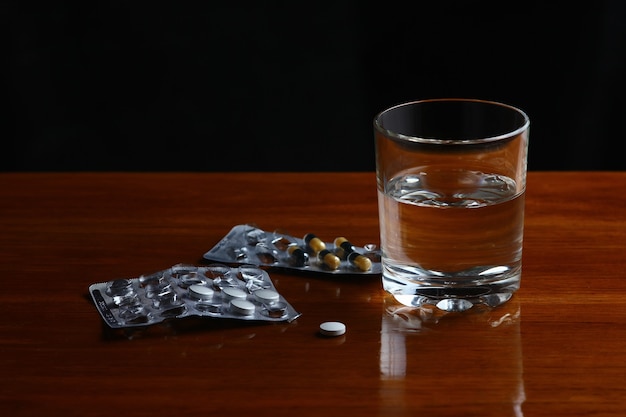 a glass of water with medical pills on the table