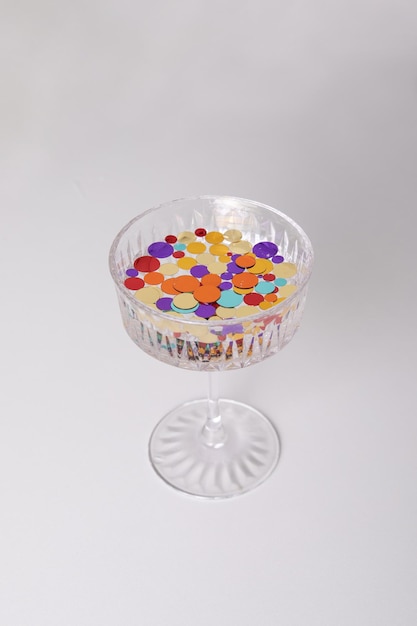 Glass of water with multicoloured confetti on white background