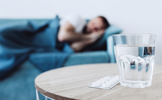 Bicchiere d'acqua con pillole sullo sfondo di un uomo malato addormentato