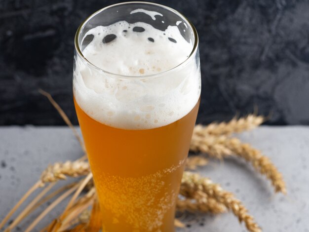 Foto un bicchiere di birra di grano su uno sfondo di cemento scuro e spighe di grano