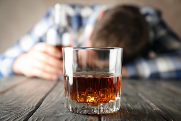 Стакан виски против пьяного человека на деревянном фоне, крупным планом