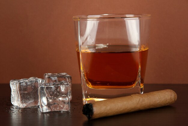 Glass of whiskey and cigar on brown