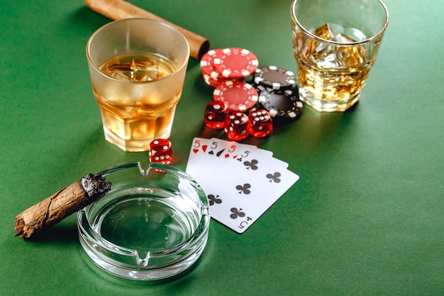 Glass of whiskey cigar playing cards and chips on green surface