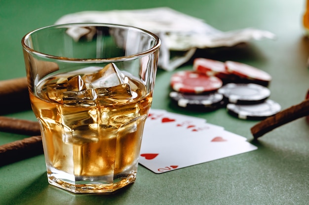 Glass of whiskey cigar playing cards and chips on green surface