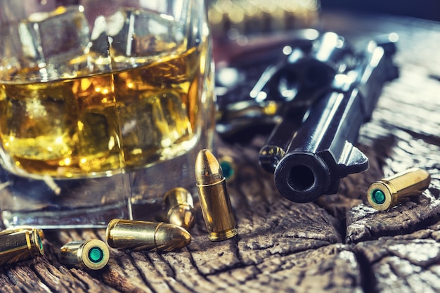 Glass of whiskey cognac or bourbon with revolver and bullets on