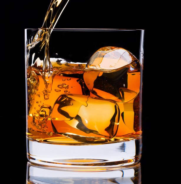 Photo a glass of whiskey and ice on a black background