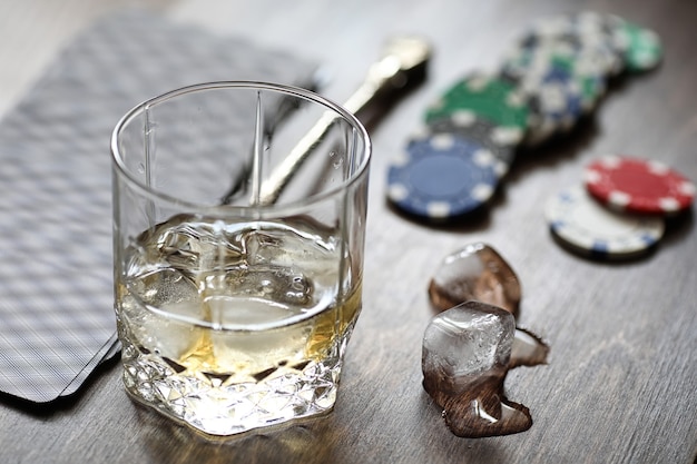 A glass of whiskey and ice on the playing table with chips and cards