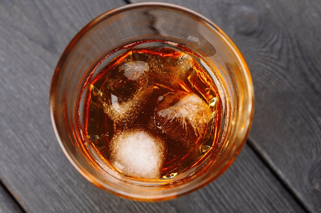 Glass of whiskey on ice with bottle on wood bar