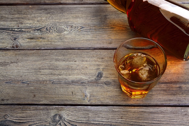 Glass of whiskey on ice with bottle on wood bar