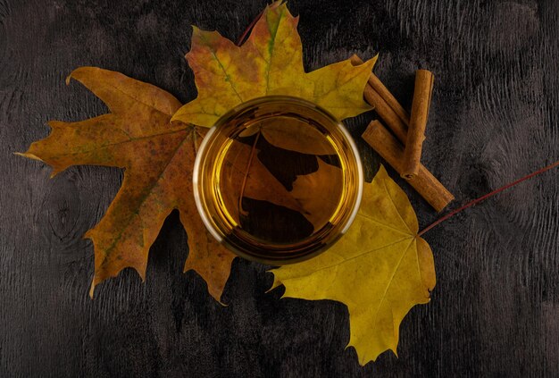 A glass of whiskey on maple autumn leaves with cinnamon