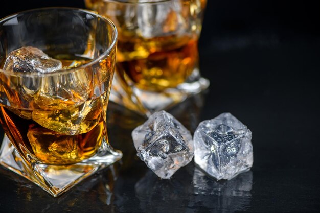 Photo glass of whiskey or other alcohol with cube ice on black background