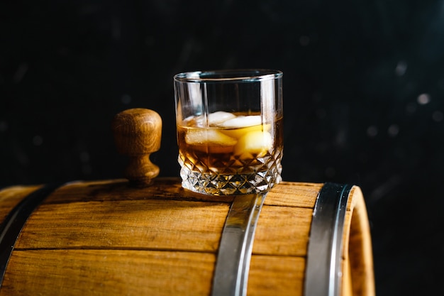 A glass of whiskey sitting on a wooden barrel