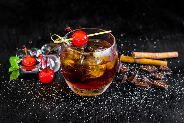 Glass of whiskey with ice and cherry on black background