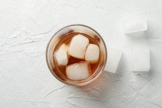 Glass of whiskey with ice cubes on white background, top view