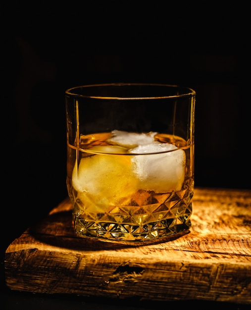 Glass of whiskey with ice cubes on the wooden table