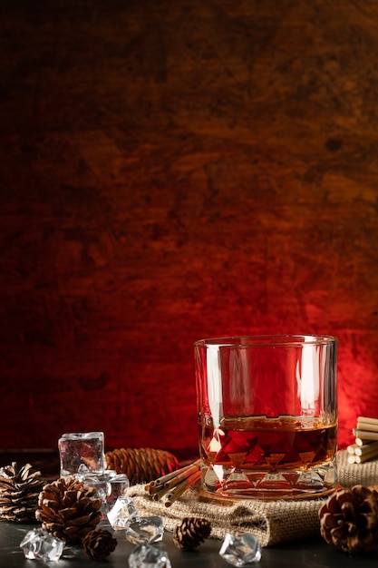 A glass of whiskey with ice on a marble black background. Glass of Scotch whiskey and ice sits on top of a rustic whiskey barrel, vertical photo.