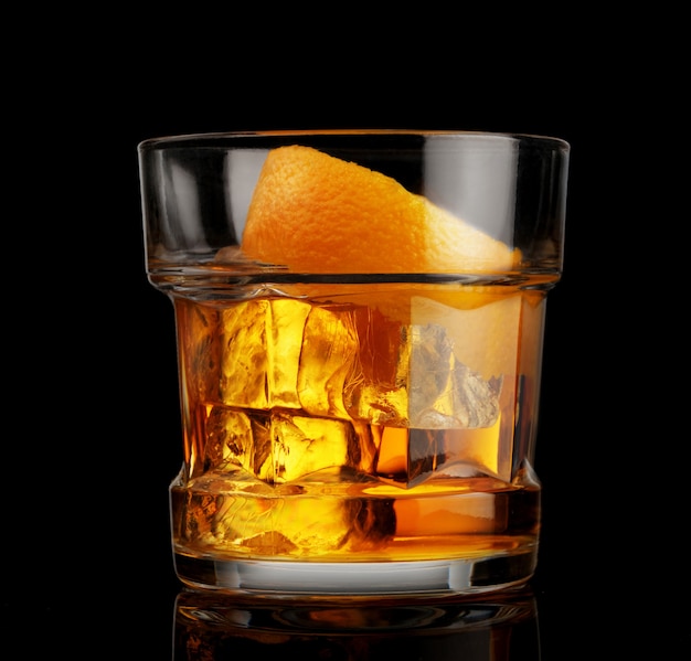 Glass of whiskey with ice and orange peel on black background