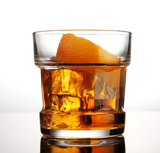 Glass of whiskey with ice and orange peel on white background