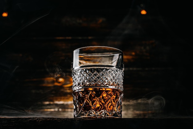 Glass of whiskey with ice on a wooden table surrounded by smoke