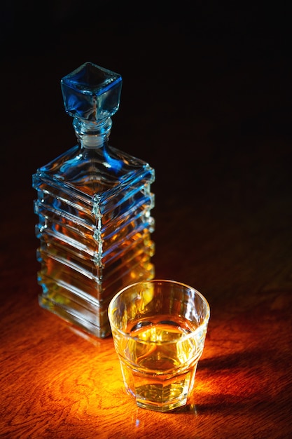 Glass of whiskey with old square carafe on a varnished wooden table