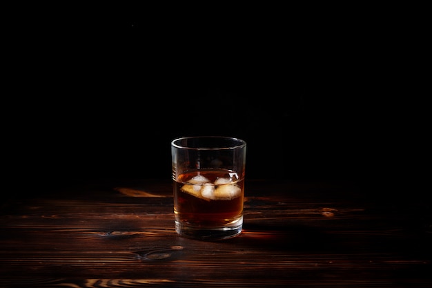 Bicchiere di whisky con fumo e ghiaccio su un tavolo di legno