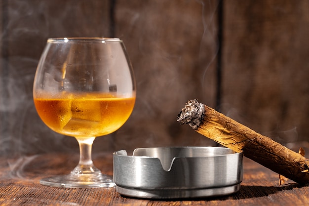 Glass of whisky and lighted cigar in an ash tray