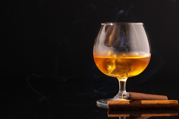 Bicchiere di whisky e sigaro acceso su sfondo nero