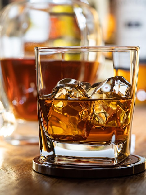 Photo glass of whisky on the rocks on a wooden bar top with bottles in the background