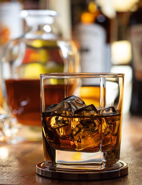 Photo glass of whisky on the rocks on a wooden bar top with bottles in the background