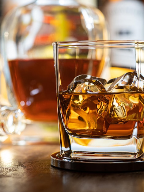 Photo glass of whisky on the rocks on a wooden bar top with bottles in the background