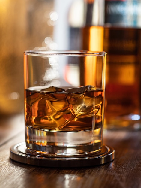 Photo glass of whisky on the rocks on a wooden bar top