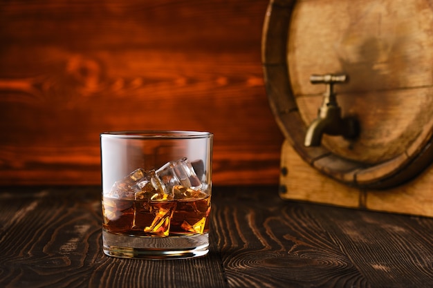 Photo glass of whisky with ice with barrel on background