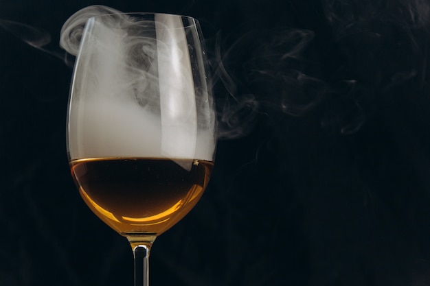 A glass of white wine on a black background. The smoke from the hookah envelops the glass.