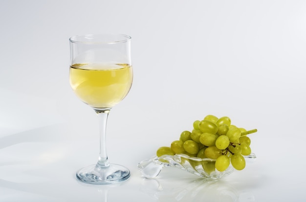 Glass of white wine and a bunch of green grapes on a glass plate