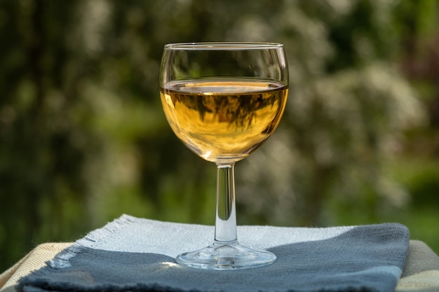 Glass of white wine over green garden background.