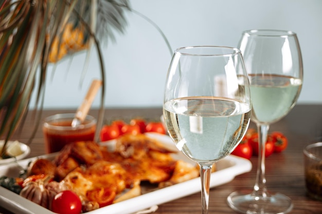 Glass of white wine and homemade food chicken tabaka with vegetables on the baking sheet on the background Dinner concept