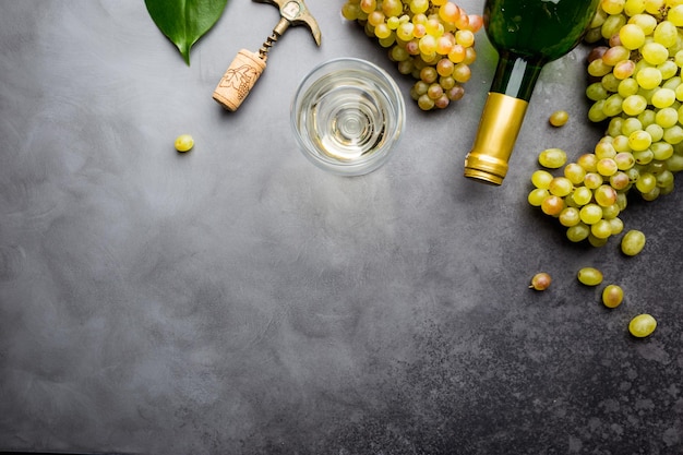 Glass of white wine and ripe grapes on gray background, top view