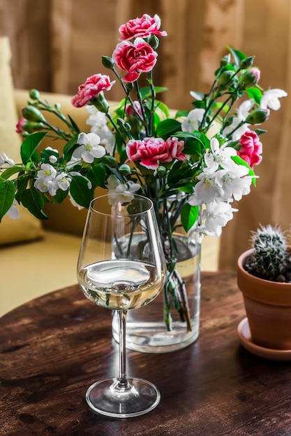 A glass of white wine and a vase of flowers on the table in the cozy living room