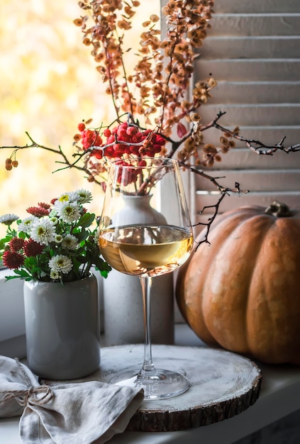 Glass of white wine on the windowsill Autumn still life with white wine chrysanthemums pumpkin on the background of the window Autumn mood still life