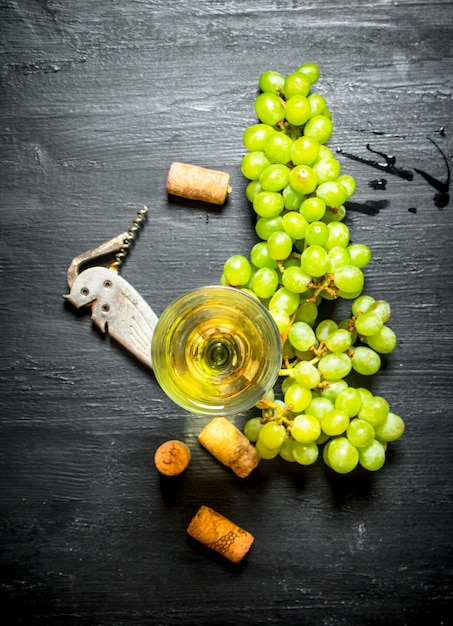 Glass of white wine with corks and bunch of white grapes.